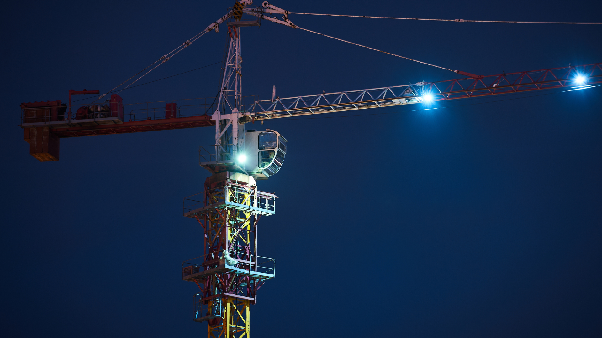 Kivilágított toronydaru éjszakai építési területen, ahol a munkavégzéshez és a biztonságos üzemeléshez folyamatos energiaellátás szükséges.